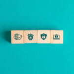 Sicherheitskonzept mit Icons auf Holzklötzchen auf türkisfarbenem Tisch – Symbolbild für digitale Absicherung, Datenschutz und Cybersicherheit.