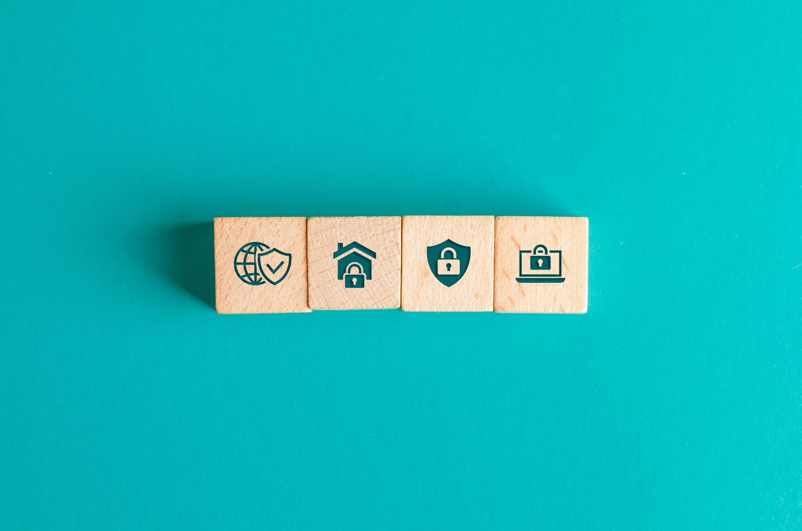 Sicherheitskonzept mit Icons auf Holzklötzchen auf türkisfarbenem Tisch – Symbolbild für digitale Absicherung, Datenschutz und Cybersicherheit.
